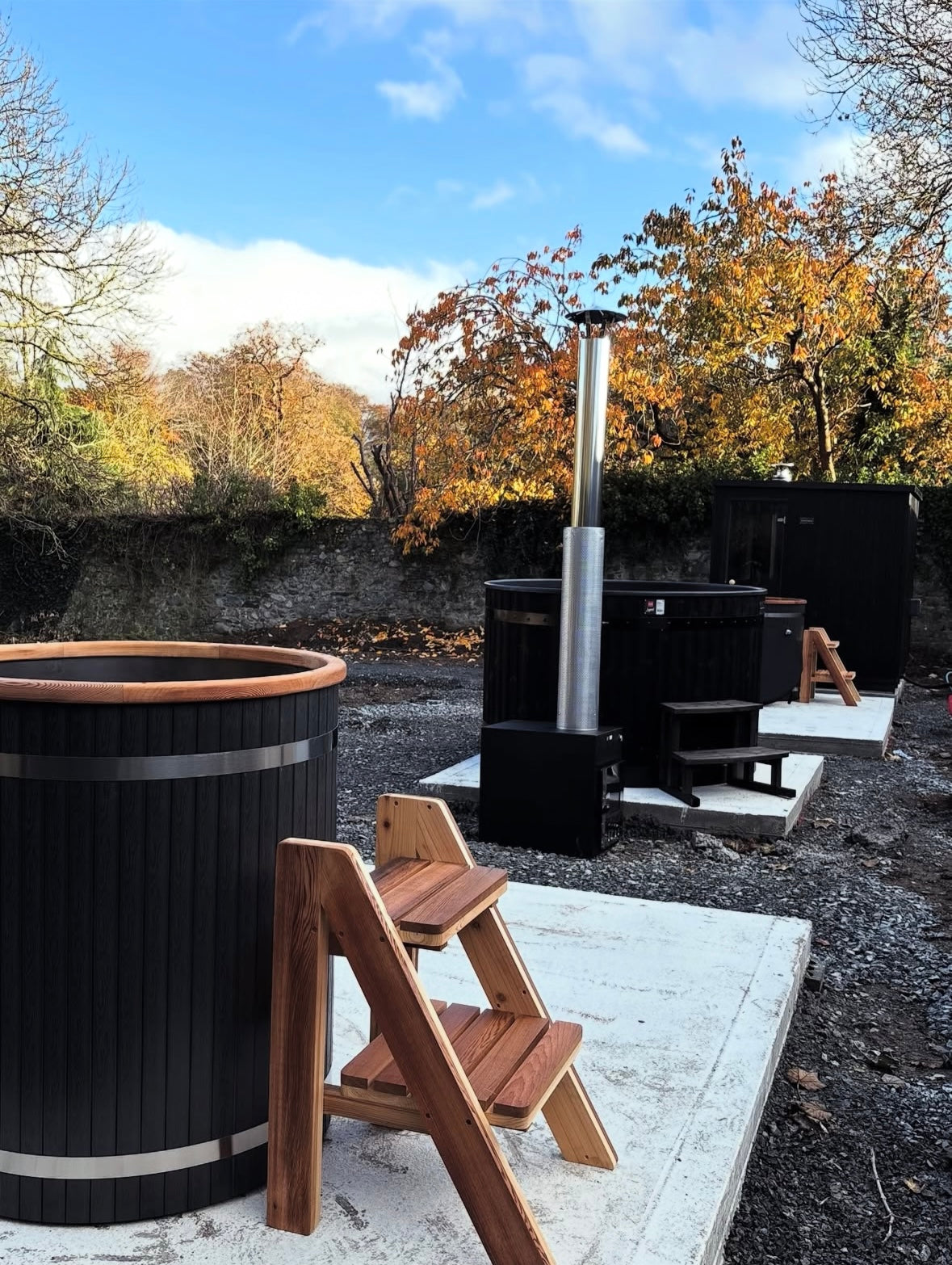 Outdoor setting with a black hot tub and wooden steps leading up to it, surrounded by trees and clear sky.